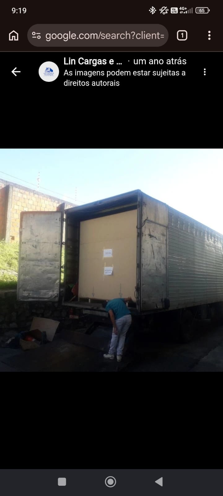 Caminhão baú com as portas abertas sendo carregado, com um painel grande protegido por papelão na entrada